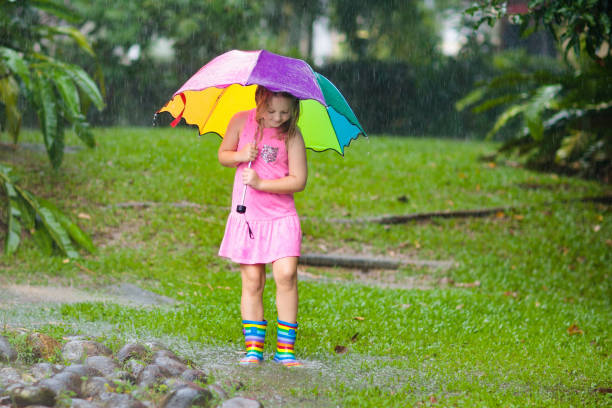 istock Kid with umbrella playing in summer rain. 1136272541
