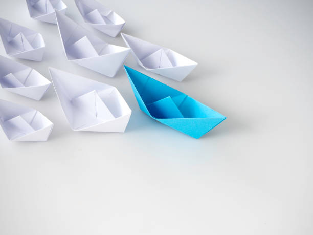 istock Blue paper boat leading among white ships 1136286086