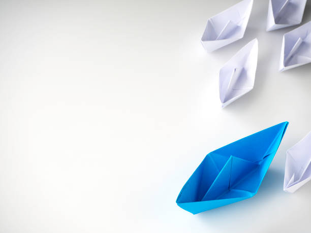 istock Blue paper boat leading among white ships 1136286371