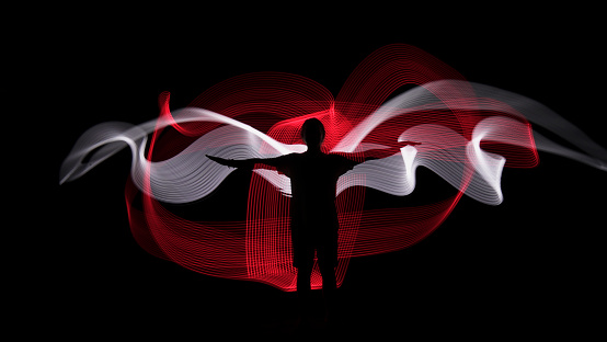 Human silhouette against red and white backlight in shape of wings. Light painting photography. Long exposure.