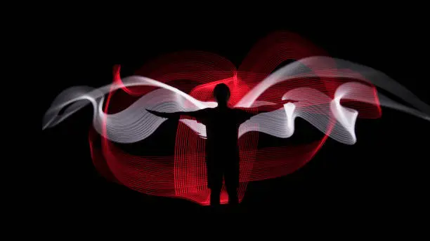 Photo of Human silhouette against red and white backlight in shape of wings. Light painting photography. Long exposure.