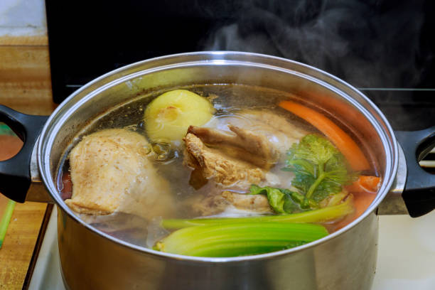 bouillon de poulet avec des morceaux de légumes dans un pot en métal avant de cuisiner avec de la soupe de poulet avec des légumes dans le processus de préparation - food heat serving size casserole photos et images de collection