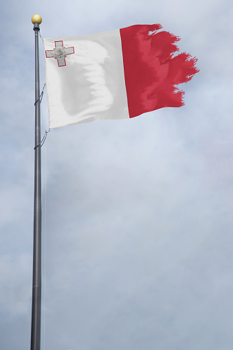 Worn and tattered Malta flag blowing in the wind on a cloudy day