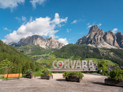 Corvara, South Tyrol, Italy - June 18, 2016: A carved, wooden sign identifies the Alta Badia town of Corvara, with Dolomites peaks in the background.