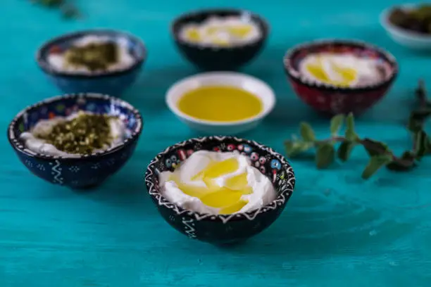 Photo of labneh (labaneh) middle eastern soft white goat's milk cheese with olive oil ,olives ,  za'atar , lemon, on blue wooded background