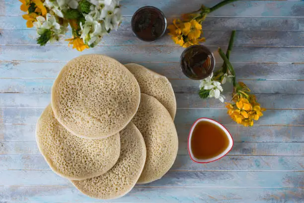 Moroccan pancakes Baghrir or crapes with 1000 holes served with honey, tea with nana , with background with flowers top view , flatlay with copy space