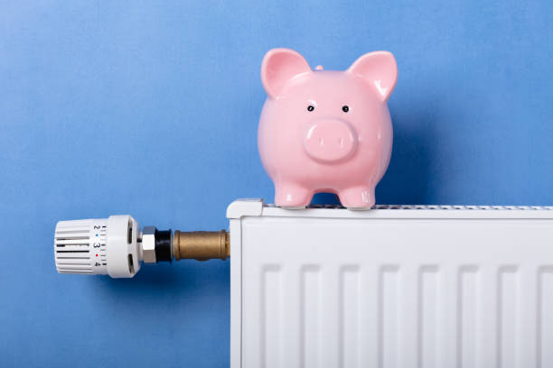 Piggy Bank On Heating Radiator With Temperature Regulator Against Blue Background