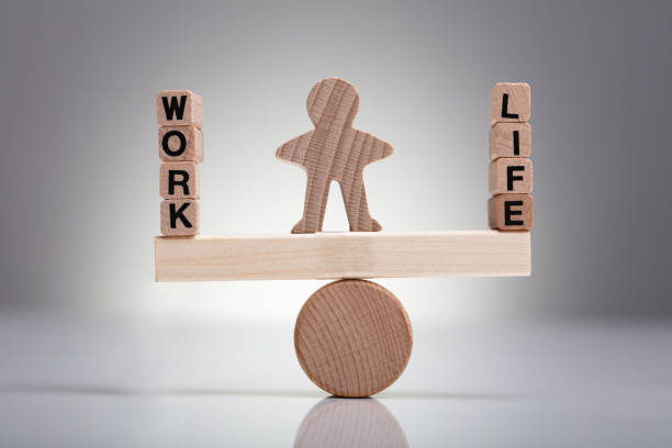 Human Figure Balancing Between Work And Life On Wooden Seesaw Against Gray Background
