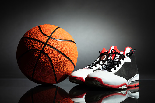 Pair Of Sport Shoes And Basketball On Desk Against Black Background