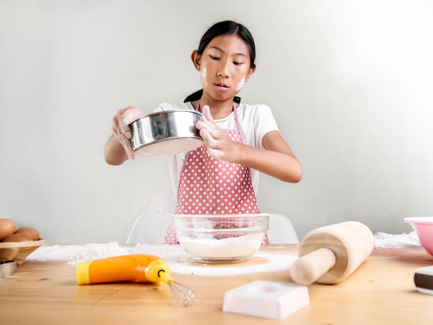 istock Asian girl sprinkling powder flour in bowl, bakery processing. 1136317396