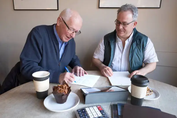 Photo of Senior Man Signing Contract During Breakfast Meeting in Coffee Shop