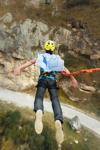 Photo of A man in a helmet jumps ropeup with an empty flag in the mountains. Extreme sports. Leisure. Top view