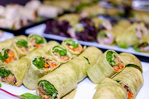 Canapes in unique green wraps consisting of mostly vegetables. These healthy meal items are sliced and placed on a serving plate. A catering concept.