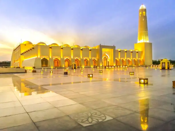 Scenic Doha Grand Mosque with minaret illuminated, mirrors on the outdoor marble pavement. Qatar State Mosque, Middle East, Arabian Peninsula in Persian Gulf. Twilight shot.