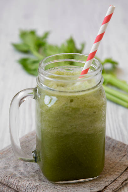 istock Green celery smoothie in glass jar over white wooden surface, side view. Close-up. 1136340325