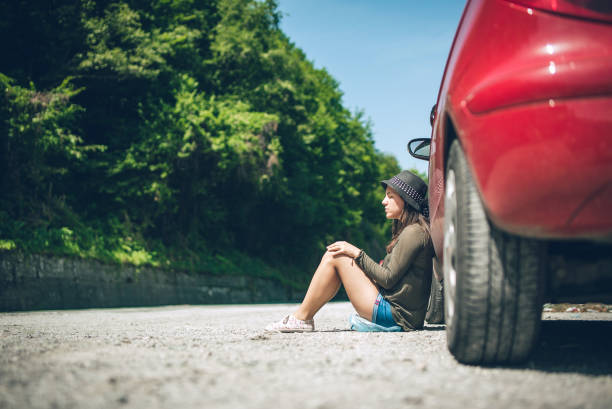 donna seduta vicino a un'auto distrutta - vehicle breakdown car stranded women foto e immagini stock