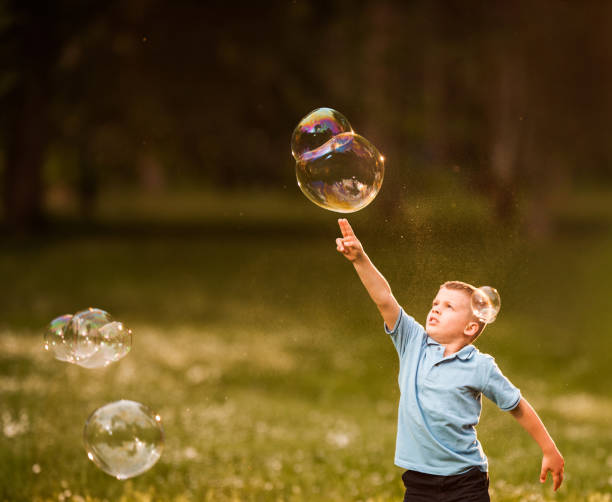 istock Little boy having fun while splashing rainbow bubbles in nature. 1136343396