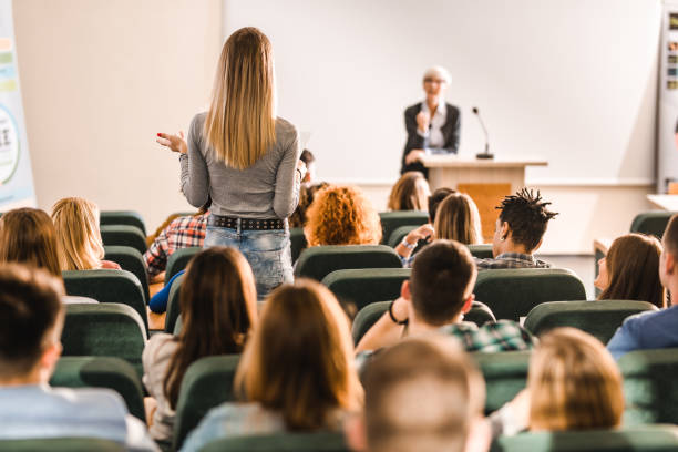 istock Back view of a female student talking to a professor on a class at lecture hall. 1136344911