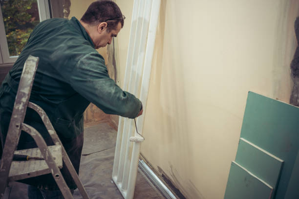istock Manual Worker with Small Paint Roller is Working on Home Improvement as he is Repainting the Radiator in Residential Building 1136344952