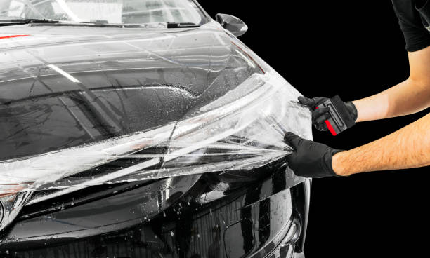 Car wrapping specialist putting vinyl foil or film on car. Protective film on the car. Applying a protective film to the car with tools. Car detailing. Transparent film. Car paint protection. Trimming stock photo