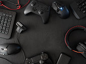 gamer workspace concept, top view a gaming gear, mouse, keyboard, joystick, headset, mobile joystick, in ear headphone and mouse pad on black table background.