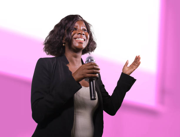 young attractive and confident black afro American business woman with microphone speaking in auditorium at corporate event or seminar giving motivation and success coaching conference stock photo