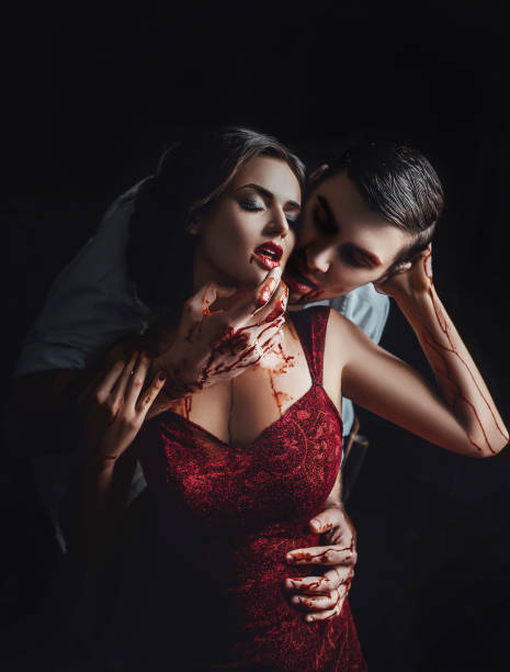 histoire d'amour sanglante passionnée avec vampire, fille et guy dans la chambre noire avec le sang écarlate sur les bras, la poitrine et le visage, des histoires effrayantes de jeu avec satan, dame sexy en robe rouge et l'homme mordant son cou - sensuality halloween witch devil photos et images de collection