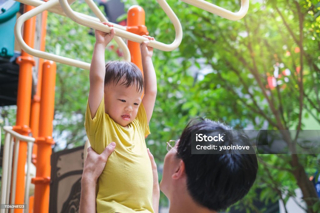 Father and Cute little Asian 2 - 3 years old toddler baby boy child having fun exercising outdoor and dad help catch up on Monkey Bars Equipmen Father and Cute little Asian 2 - 3 years old toddler baby boy child having fun exercising outdoor and dad help catch up on Monkey Bars Equipment at playground on nature at park, father's day concept Schoolyard Stock Photo