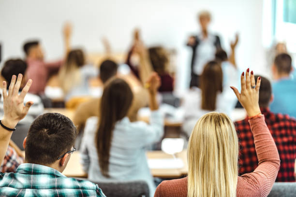 istock Back view of college students raising their arms on a class at lecture hall. 1136348194