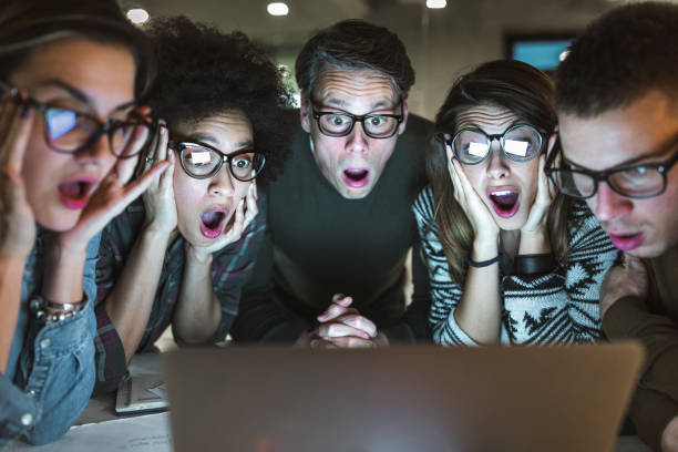Shocked team of entrepreneurs reading an e-mail on laptop in the office. Mid adult manager and his younger colleagues reading a shocking e-mail on a computer in the office. group of people wearing eyeglasses stock pictures, royalty-free photos & images