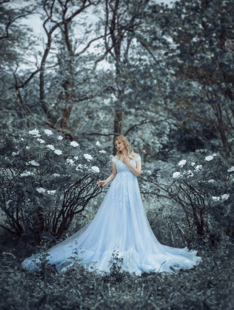 una hermosa chica rubia, un modelo de tamaño más, camina en un jardín botánico, floreciente en el telón de fondo de una peonía pionera. la chica tiene un lujoso vestido azul exuberante, como una princesa. foto de arte - tropical rainforest rainforest tropical climate formal garden fotografías e imágenes de stock