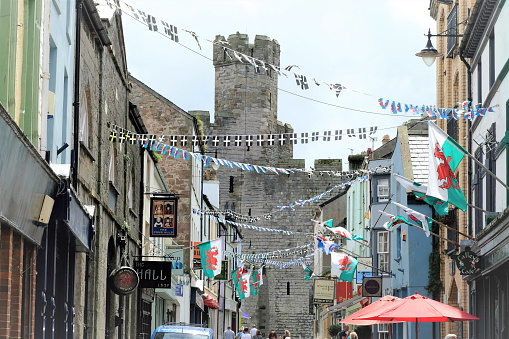 Caernarfon, Wales, UK. July 21, 2016. Tourists and sightseers walking down a street with flags and bunting towards the historic castle at Caernarfon in Wales, UK.