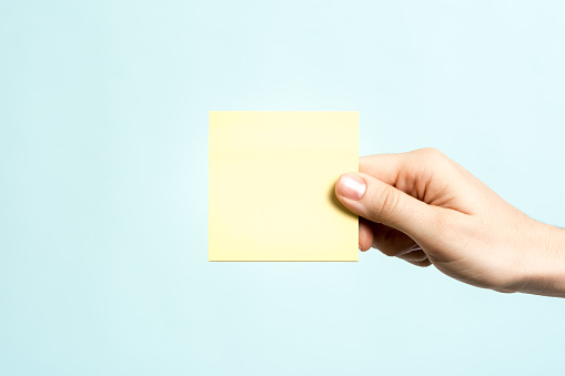 Only one hand showing a yellow empty adhesive note on blue background. Message concept.