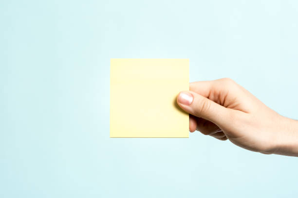 Only one hand showing a yellow empty adhesive note on blue background. Message concept. stock photo