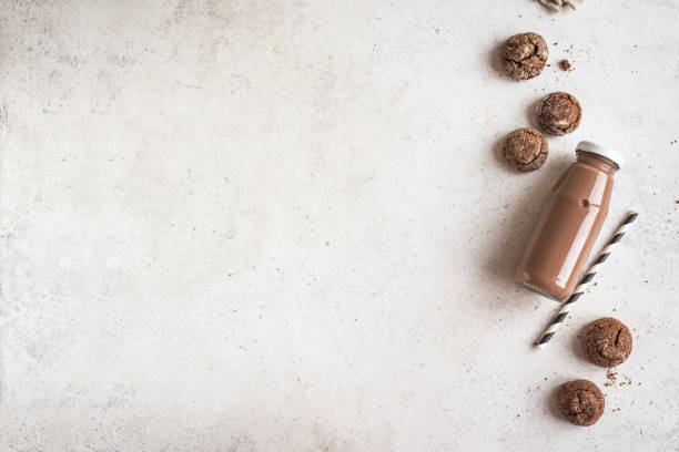 Homemade chocolate biscuit muffins next to bottle of milk on isolated background. Three homemade chocolate and cookie cupcakes next to a bottle of milk on white background