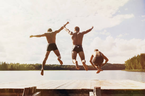diversión de verano. amigos saltando del embarcadero al lago - teenager team carefree relaxation fotografías e imágenes de stock