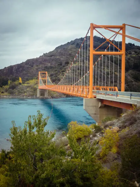 Red suspension bridge over the water runoff of General Carrera Lake, near Lake Bertrand, Puerto Tranquilo, Chile Chico, Aysen, Chile