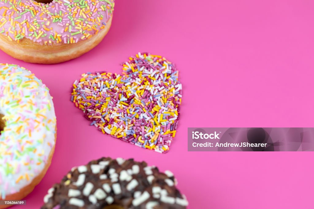 Doughnuts and Sprinkles Various doughnuts photographed on a vibrant pink background with a heart made of sprinkles. Doughnut Stock Photo