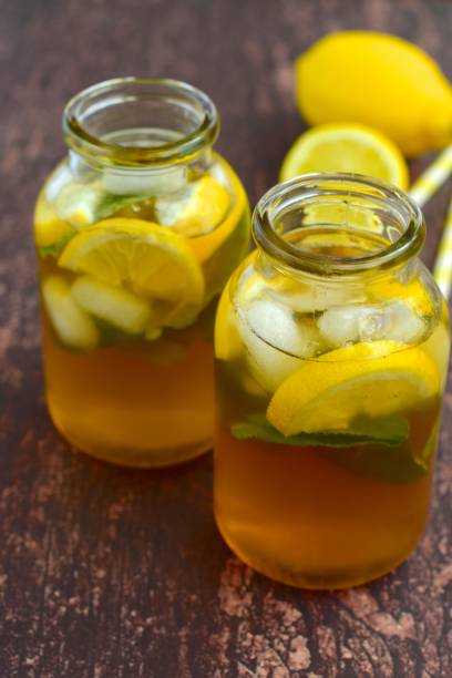 Lemon iced tea with mint leaf in jars on wooden background