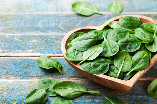 Baby spinach leaves in bowl on rustic wooden table. Organic and healthy food.