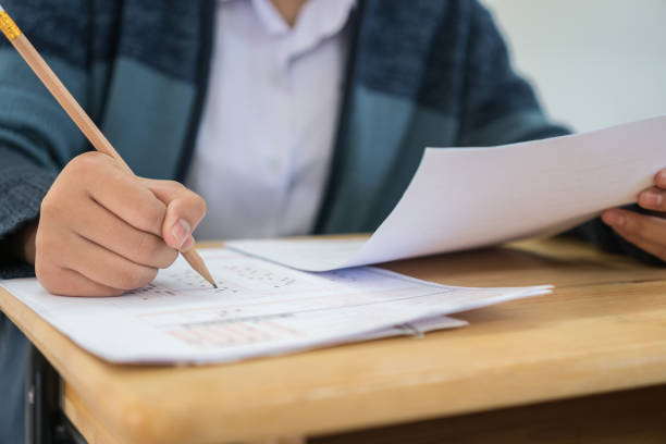istock Student taking exams, writing examination on paper answer sheet optical form of standardized test on desk doing final exam in classroom, Education assessment Concept. Soft focus 1136373979