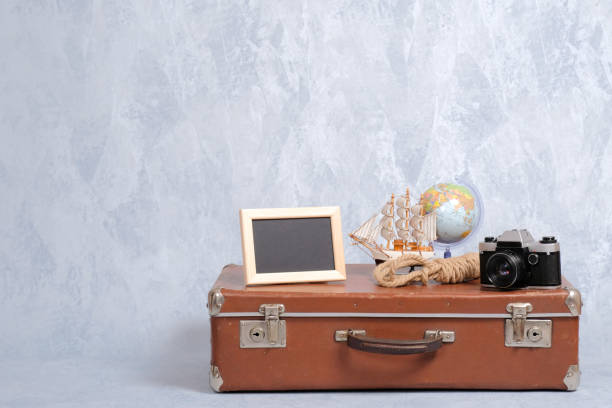 istock Shabby vintage suitcase with summer marine accessories on grey background. Picture frame, globe, camera, toy sailboat, sea rope. Travel or tourism, summer holiday, vacation concept. 1136375341