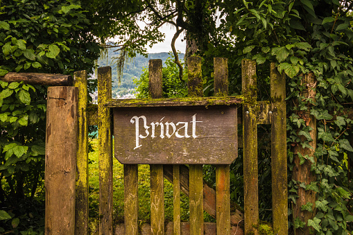 Vintage private sign in german language on an old wooden gate grown with moss and ivy and surrounded by trees.