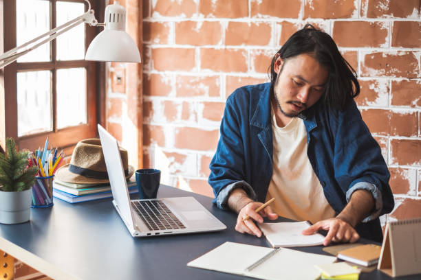 istock Young Asian man talking on phone and working on laptop for business creative designer 1136375663