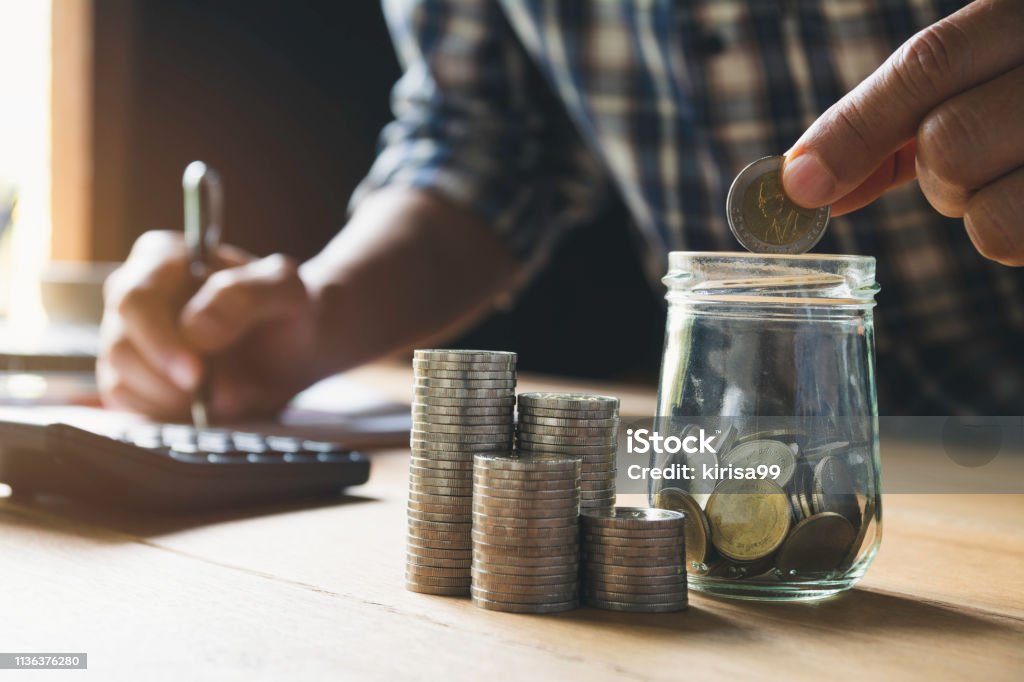 Hand putting money coin in the glass jar. Saving money, financial and accounting concept. Accountancy Stock Photo