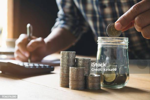 Hand Putting Money Coin In The Glass Jar Saving Money Financial And Accounting Concept Stock Photo - Download Image Now