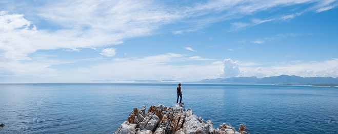 A woman stands on the rocks overlooking the beautiful sea