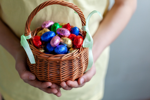 Kids hands holding basket full chocolate easter eggs, happy easter concept.