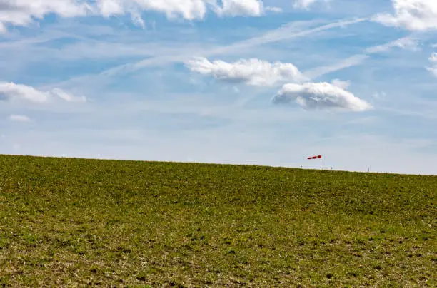 green meadow in spring with a windsock and blue sky with clouds on the horizon