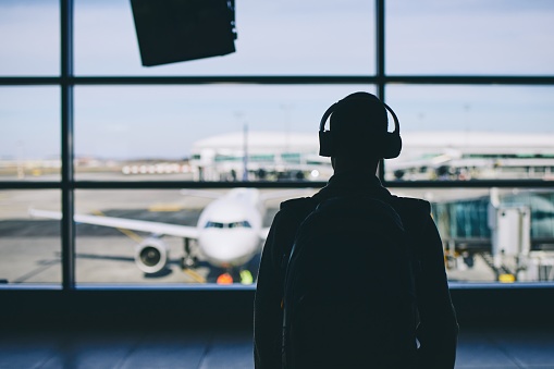 Passenger with headphones. Young man walking through airport terminal to airplane.